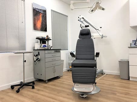 An examination room with an ENT treatment chair, an examination microscope on an arm and an instrument cart