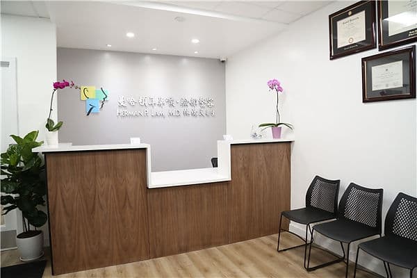 The reception desk at Manhattan ENT & Facial Plastic Surgery, with the practice's bilingual signage on the wall and framed certificates beside it